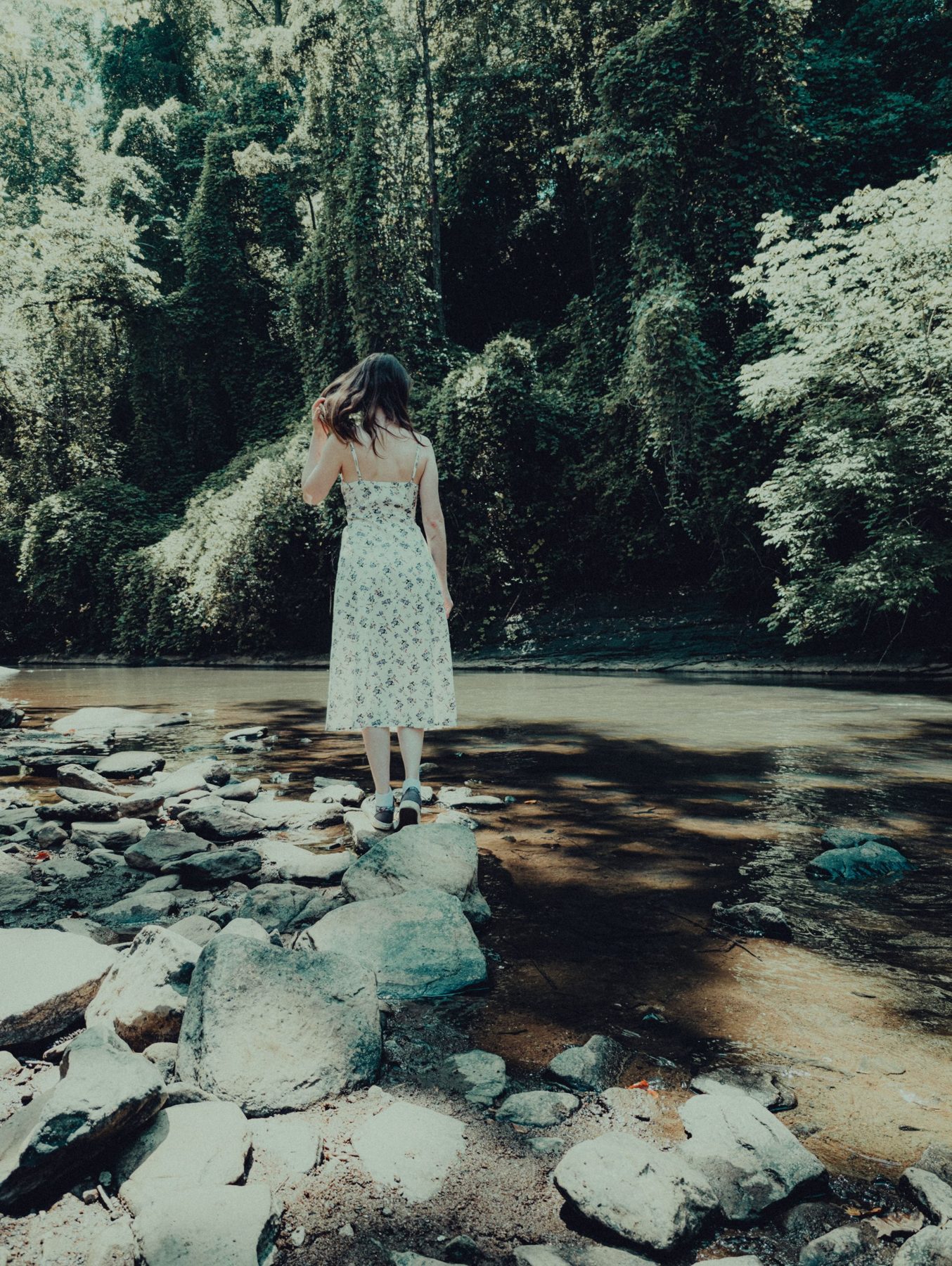 A woman in a summer dress standing on river stones in a green forest